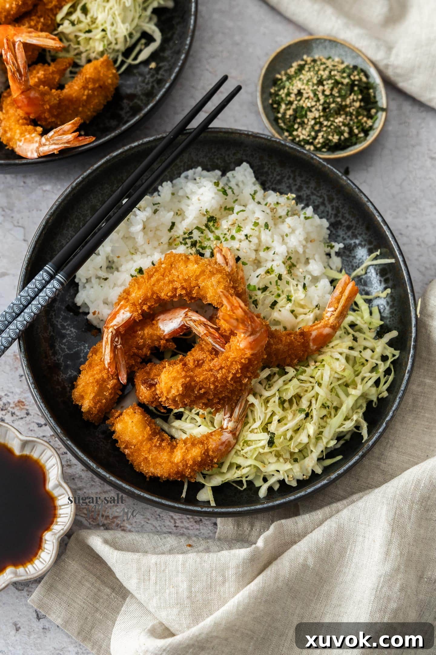 Top down view of a plate with fluffy rice and shredded cabbage, beautifully topped with crispy prawn katsu.
