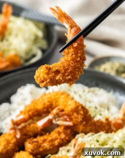 Chopsticks holding a panko crusted prawn katsu above a plate of more, illustrating the crispy texture.