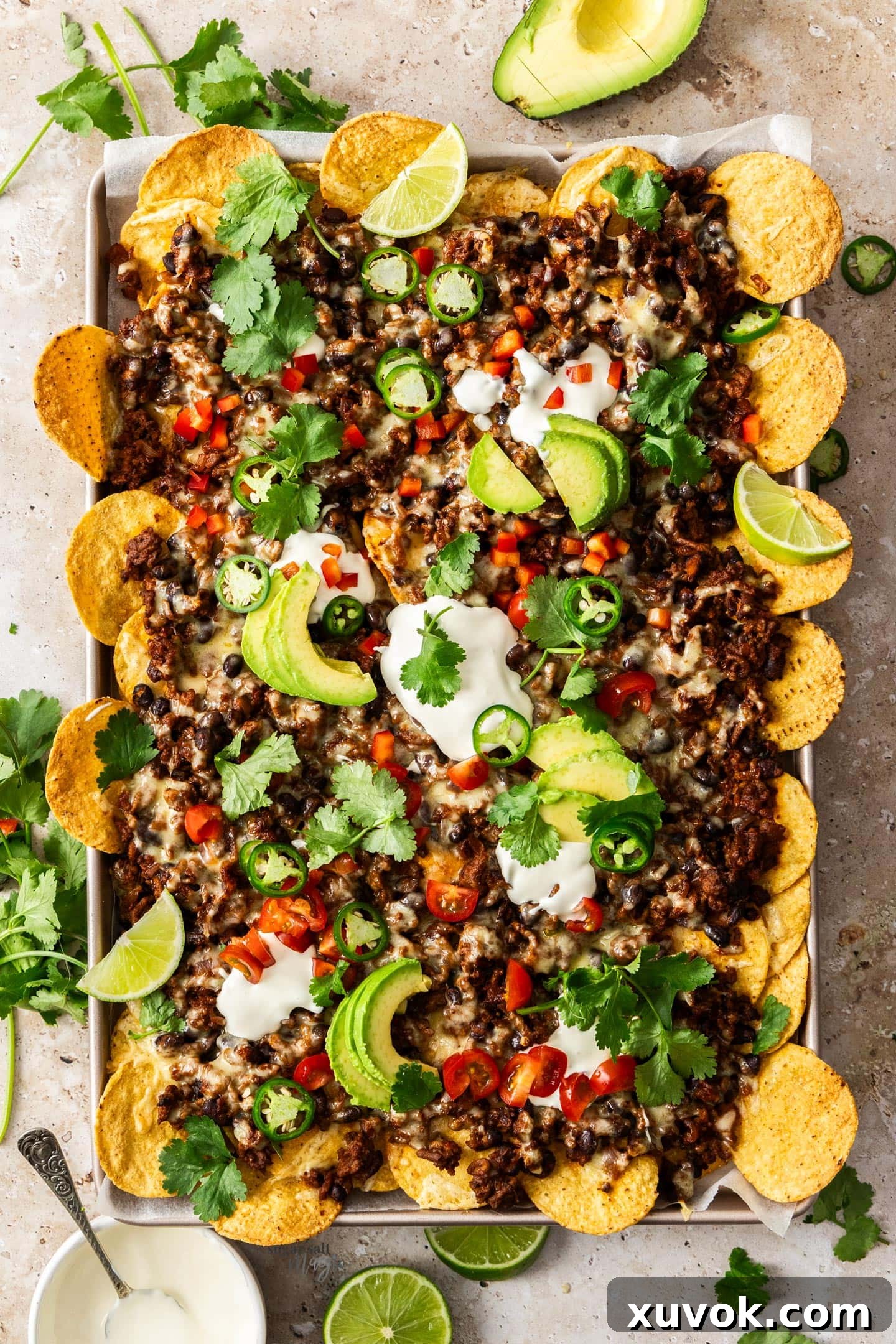 Top down view of a large pan of sizzling chilli beef nachos, generously topped with melted cheese and fresh garnishes, ready to serve.
