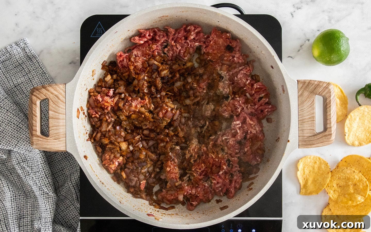 Ground beef cooking in a pan, pressed down to create a browned crust, with onions and spices pushed to one side.