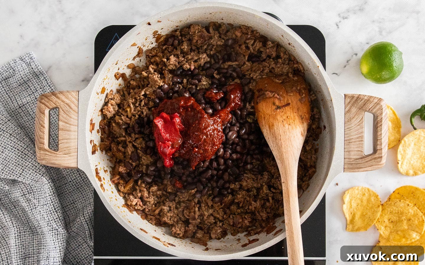 Black beans, chipotle in adobo, and tomato paste being added to the browned ground beef mixture in a pan.
