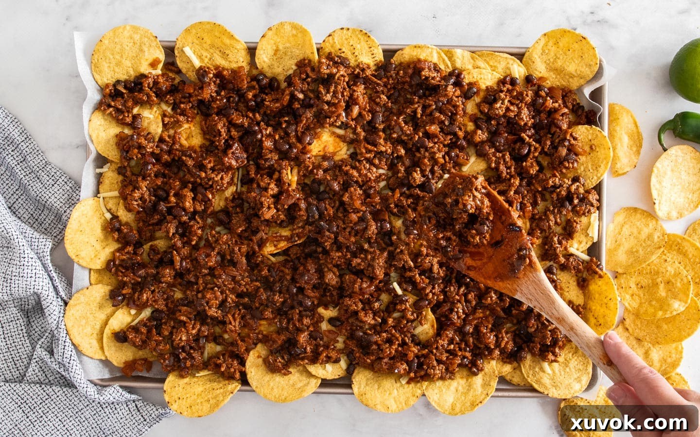 Spreading the rich chilli beef mixture over a bed of tortilla chips and a layer of cheese on a baking sheet.
