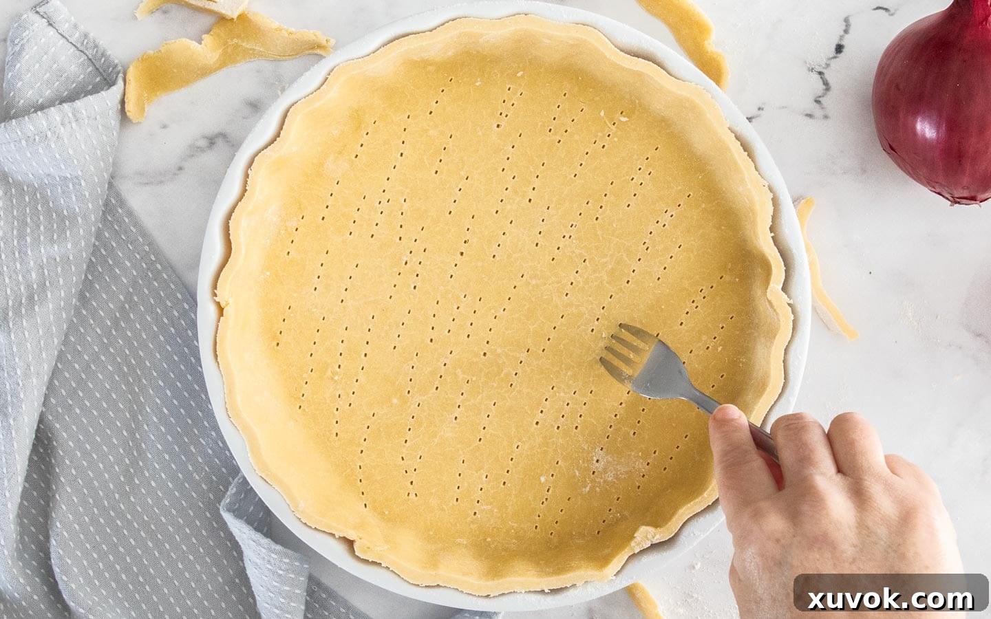 A blind-baked quiche pastry shell in a dish, with its base pricked with fork holes to prevent puffing during baking.