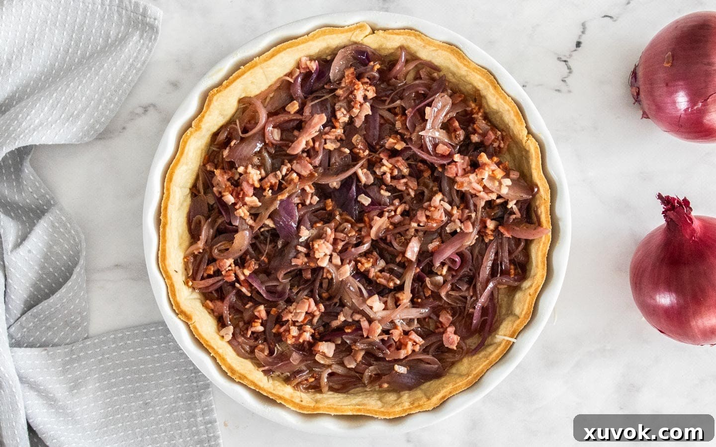 The blind-baked quiche shell filled with a generous layer of caramelized onions and crispy bacon, ready for the egg mixture.