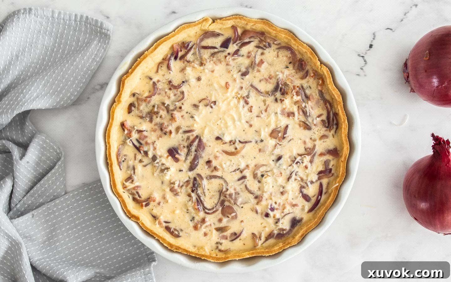 The quiche shell with the creamy egg mixture poured over the bacon, onions, and cheese, ready for baking.
