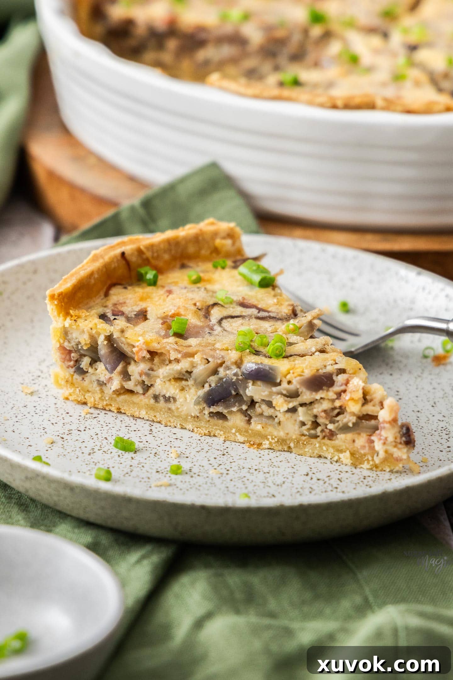A delectable slice of Bacon and Caramelised Onion Quiche elegantly presented on a white dinner plate, garnished with fresh herbs, ready to be enjoyed.