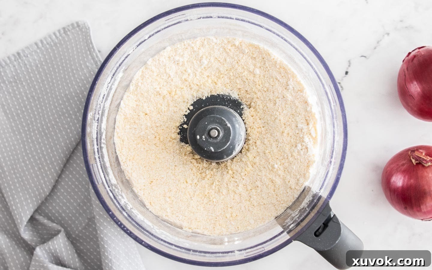 Close-up view of the pastry mixture in a food processor after the egg has been incorporated, showing a coarse, breadcrumb-like texture.