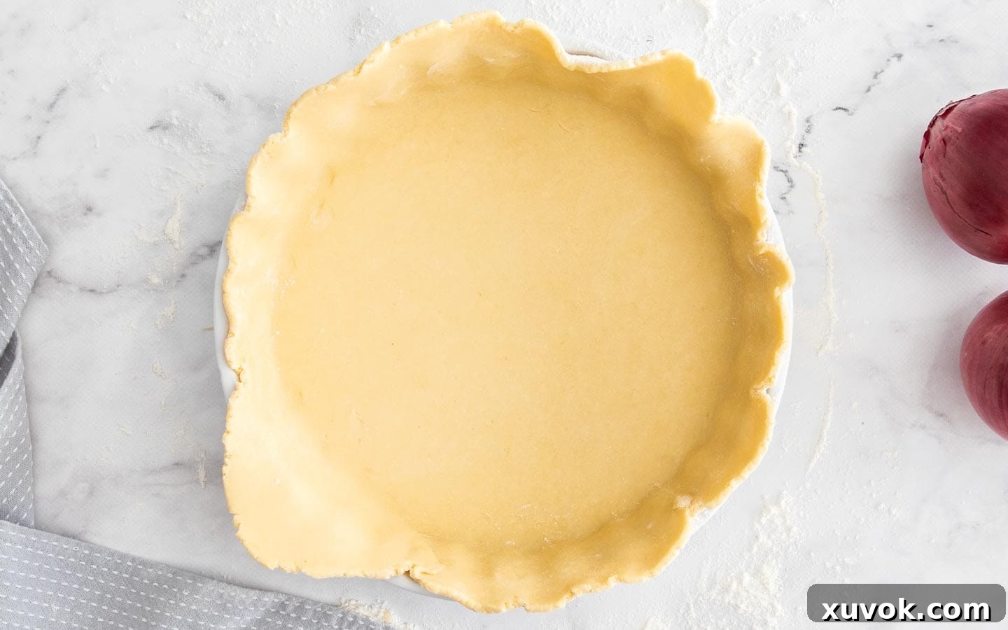 The quiche pastry dough neatly rolled out and lining a ceramic quiche dish, with a slight overhang, ready for chilling.
