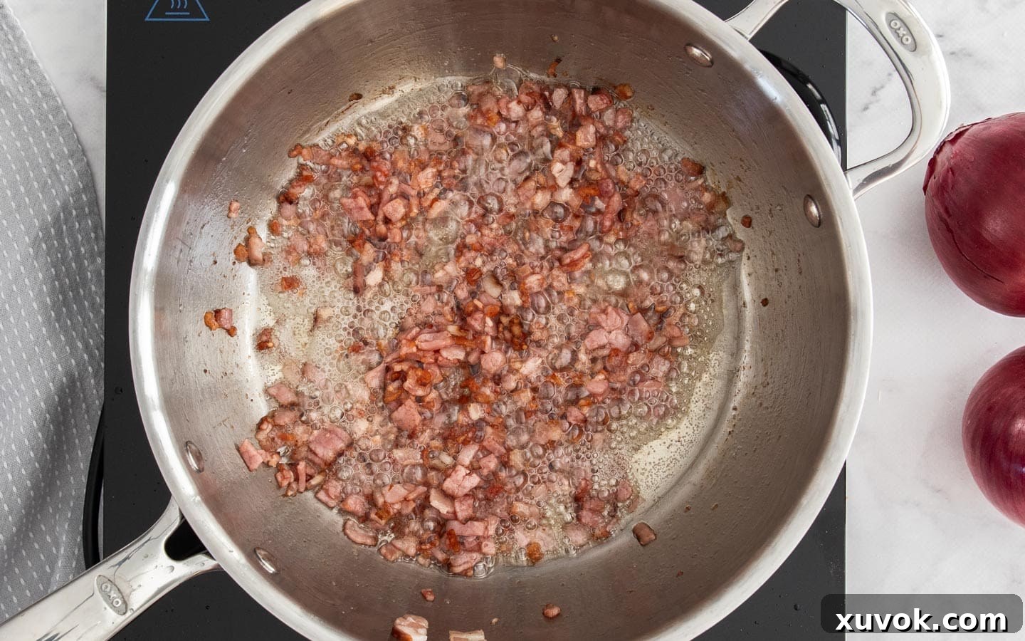 Finely diced bacon sizzling and turning golden brown in a hot pan, releasing its savory aroma and fat.