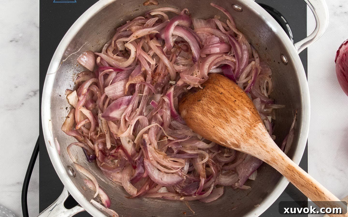 Thinly sliced red onions softened and translucent in a pan with thyme, beginning to caramelize and release their sweet aroma.