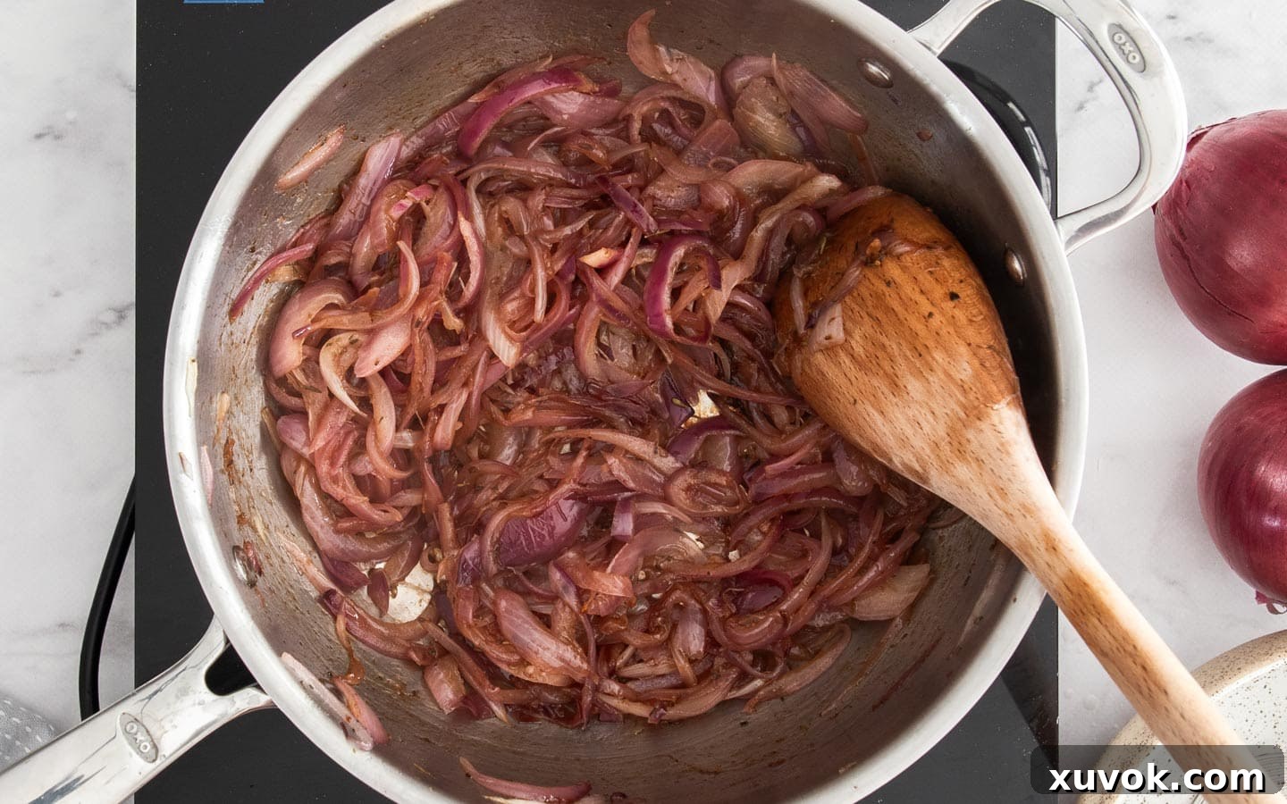 Caramelised red onions in a pan, glistening with balsamic vinegar and brown sugar, showing a rich, deep golden-brown color.