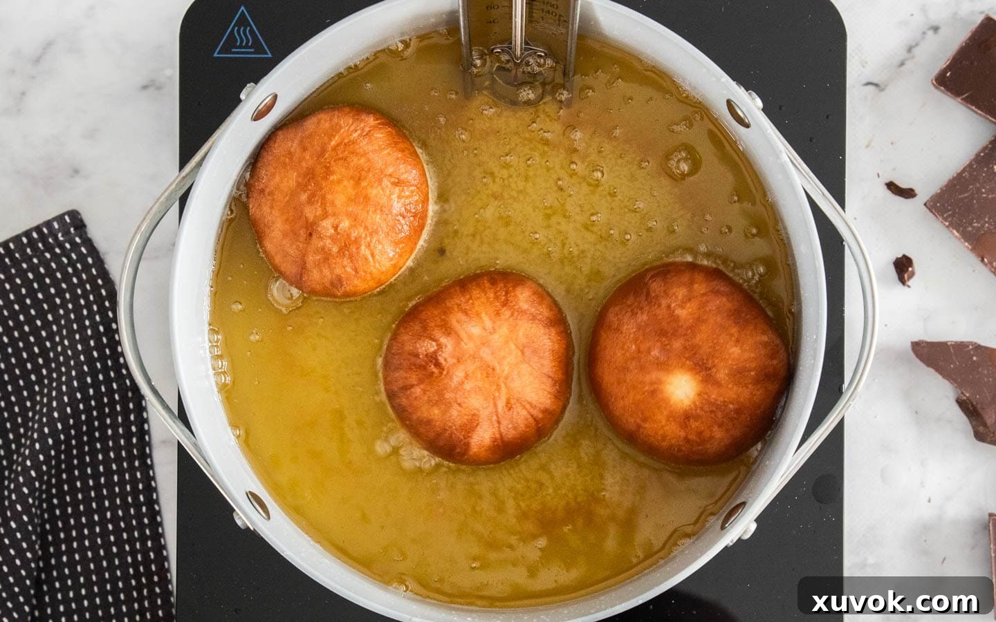 3 golden fried donuts in a pan of oil.