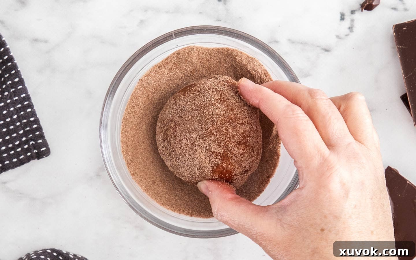 A donut being rolled in cocoa sugar.