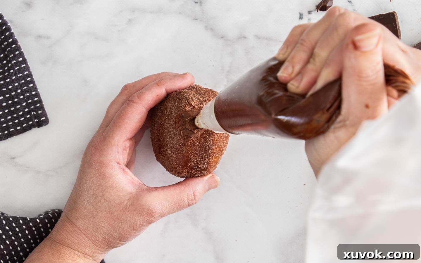 Piping ganache into a donut.