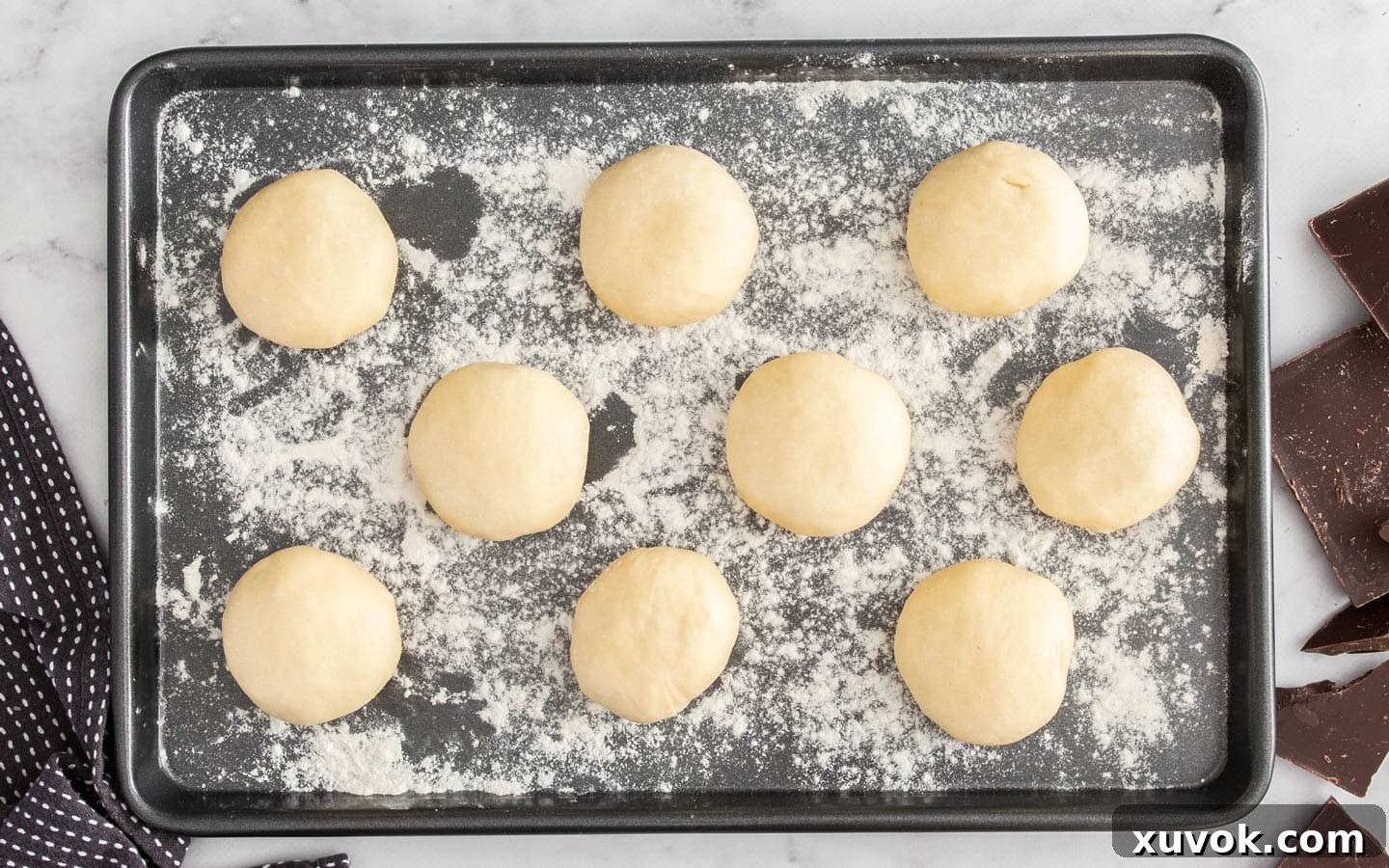 9 balls of dough on a floured baking tray.