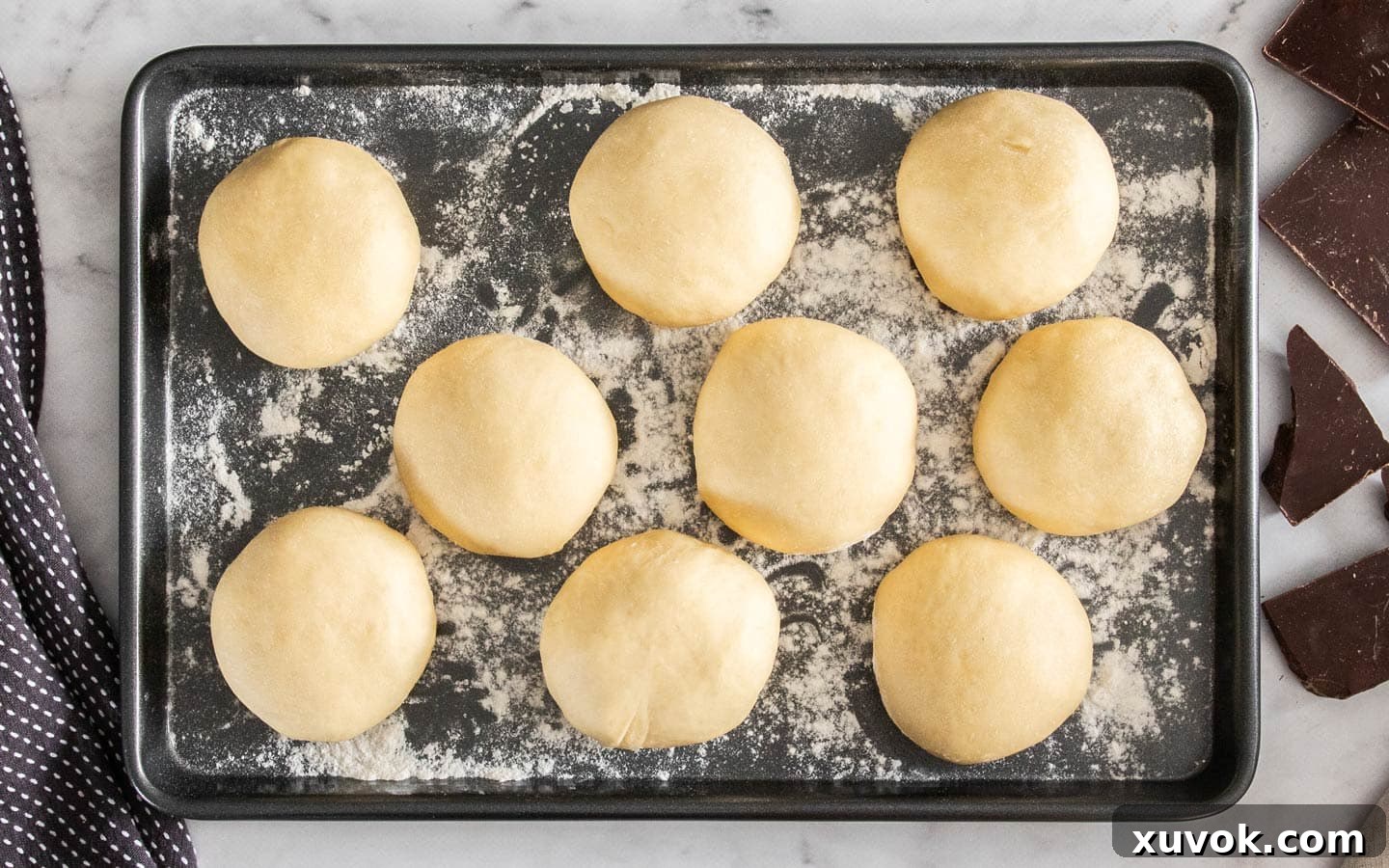 9 balls of dough on a floured baking tray after they've risen.
