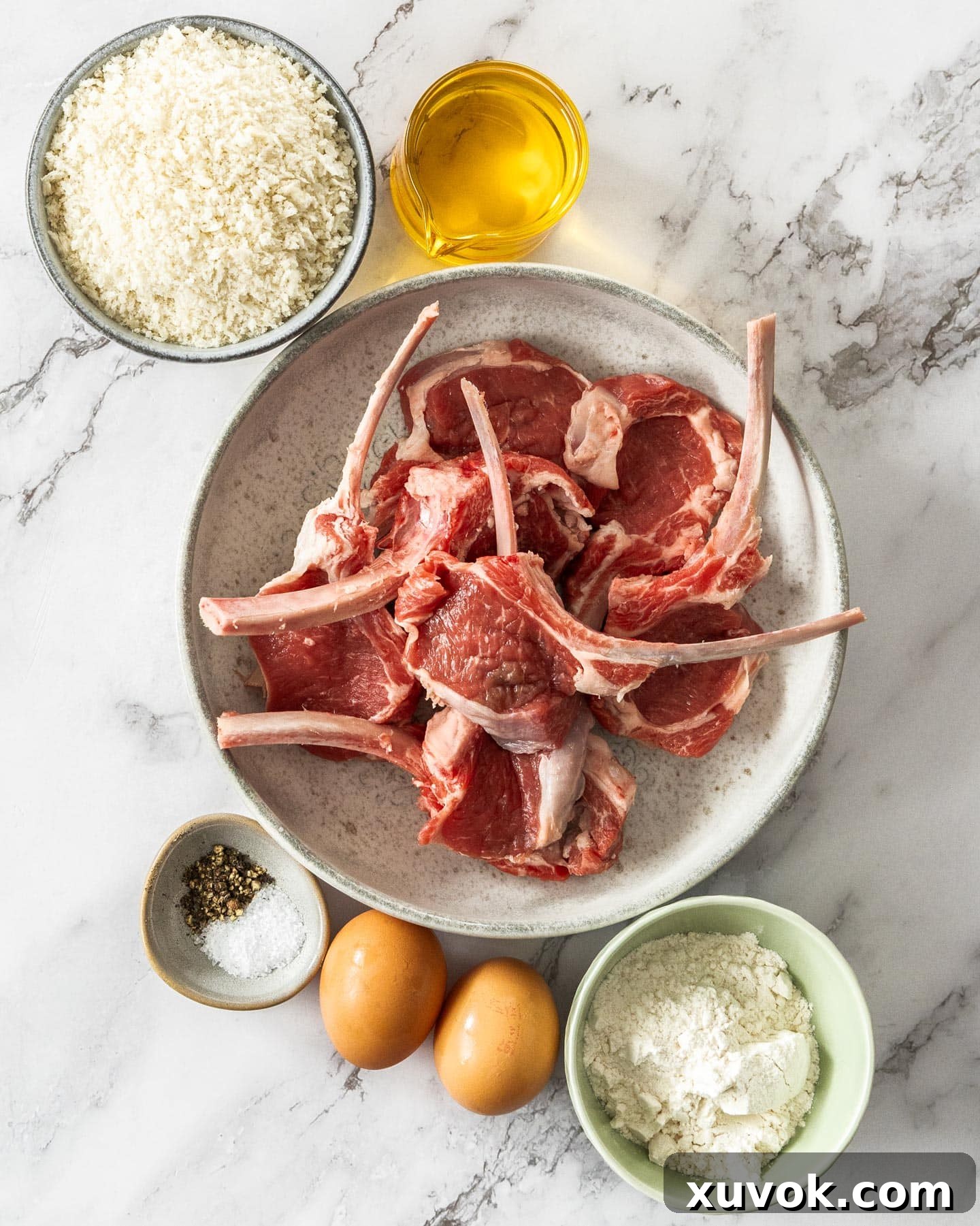Ingredients for crumbed lamb cutlets laid out on a marble surface.