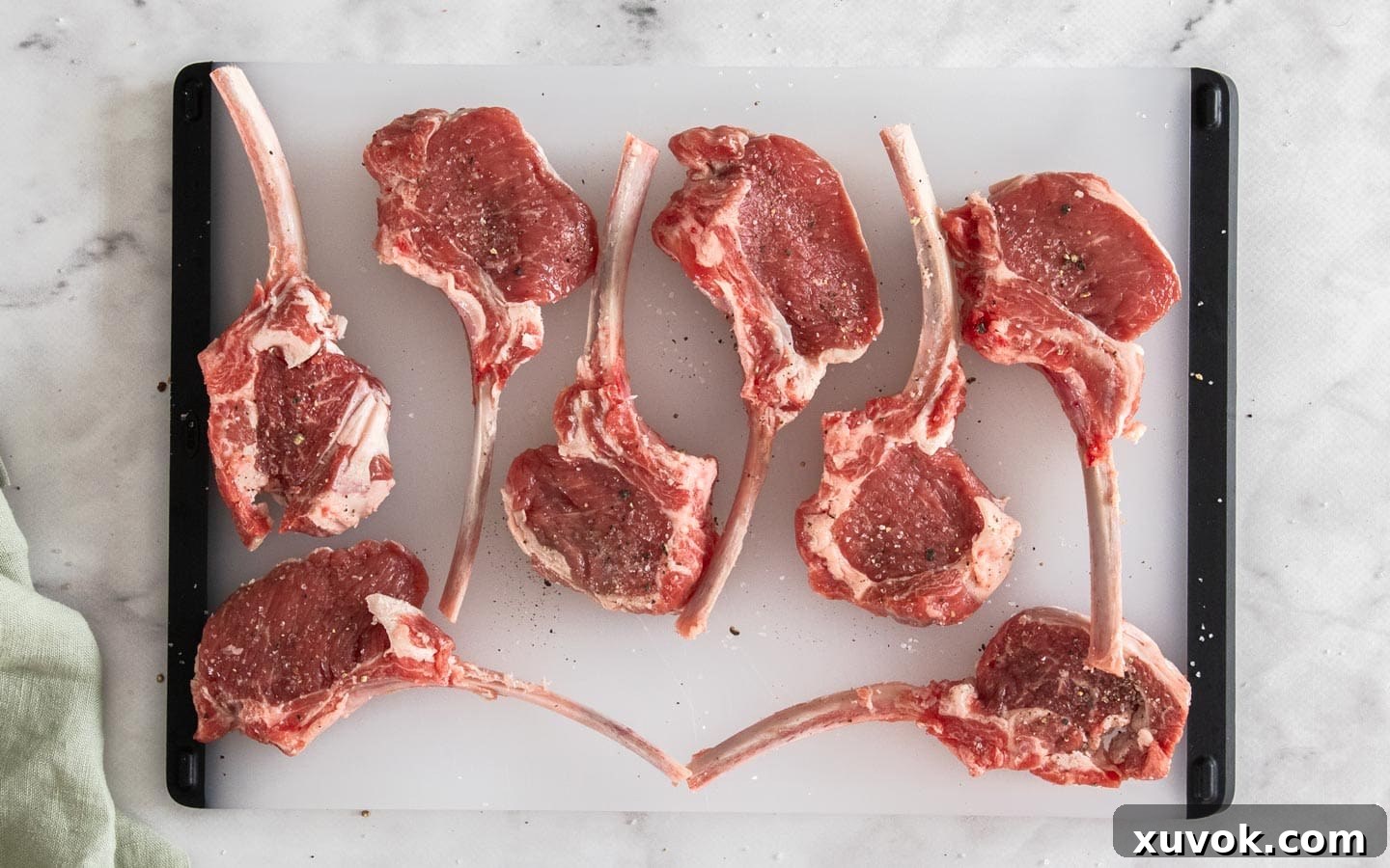 8 raw lamb cutlets neatly arranged on a chopping board, ready for preparation.