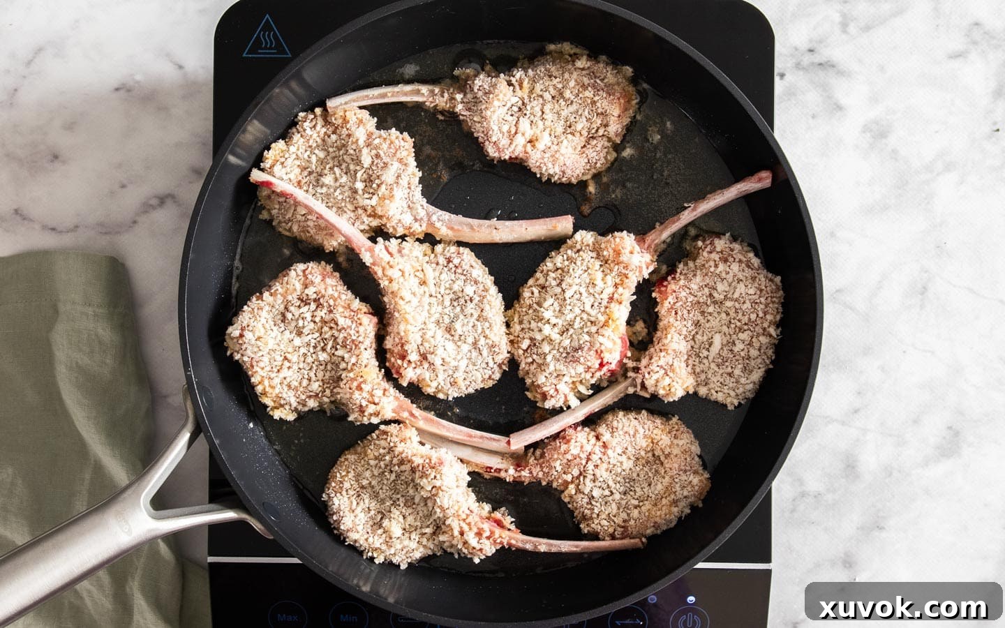 A raw crumbed lamb cutlet being gently placed into a hot frying pan with oil.