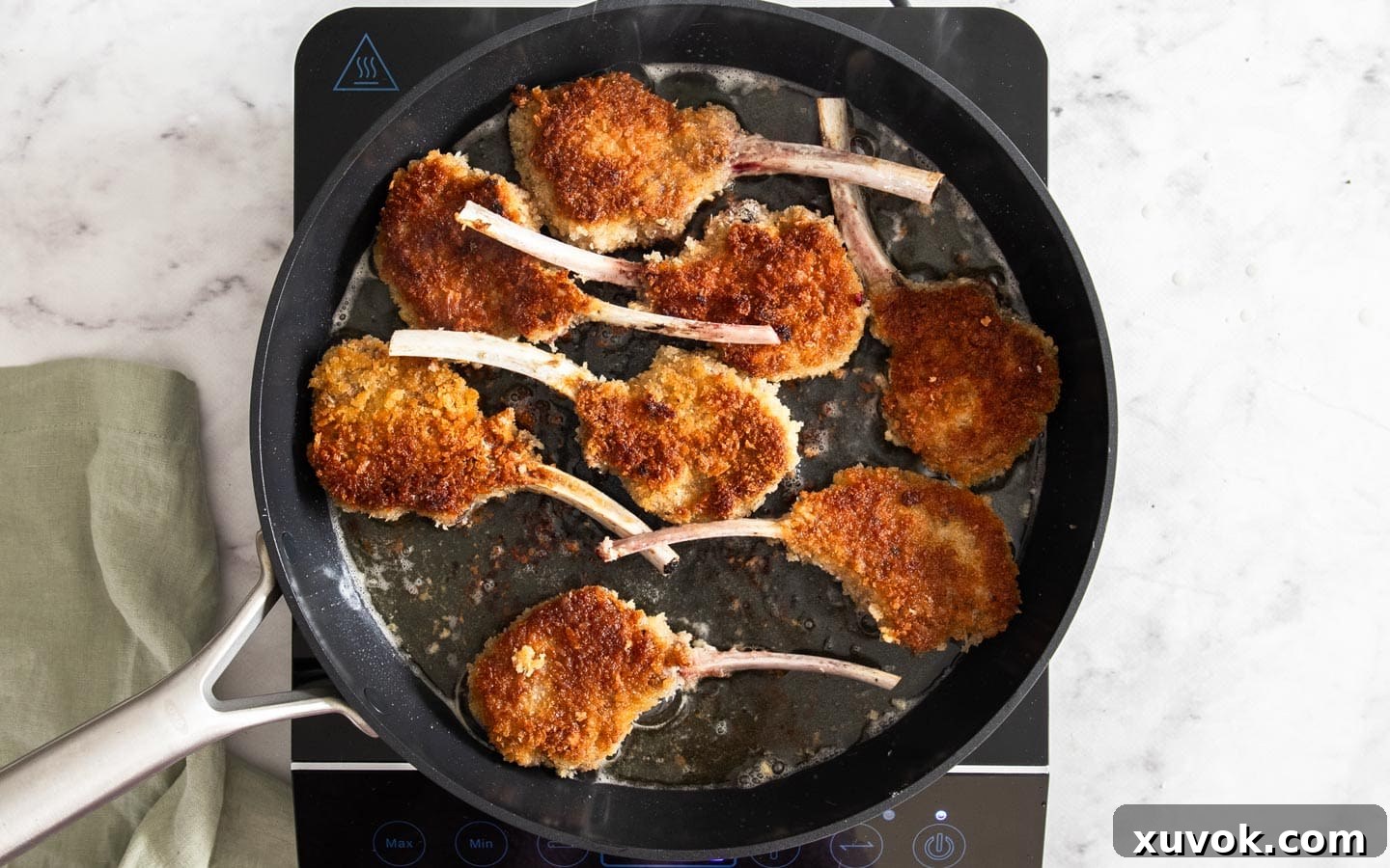 Several lamb cutlets cooking in a pan, turning golden brown and sizzling.