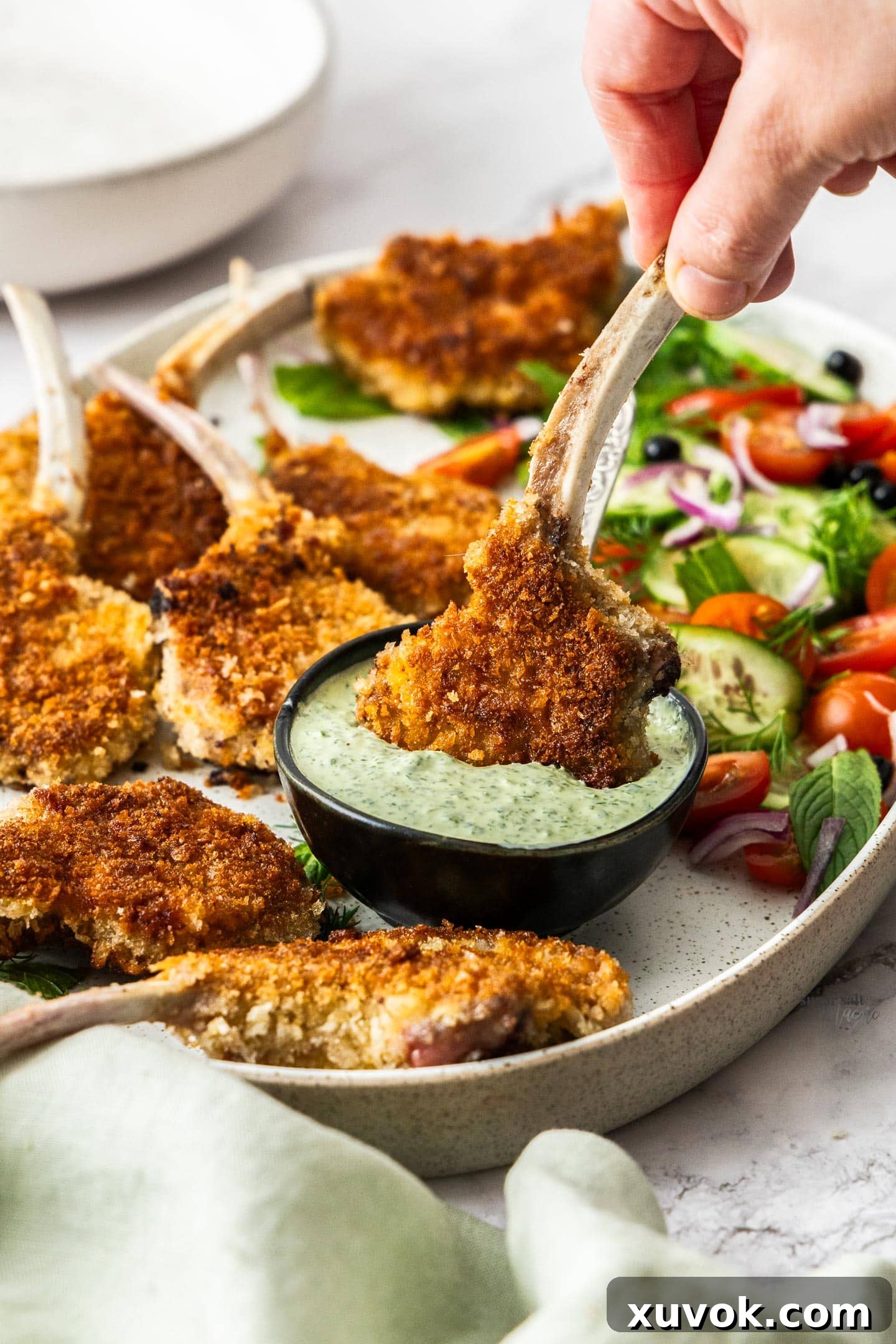 A crumbed lamb cutlet being dipped into a creamy sauce, emphasizing its crunchy texture.