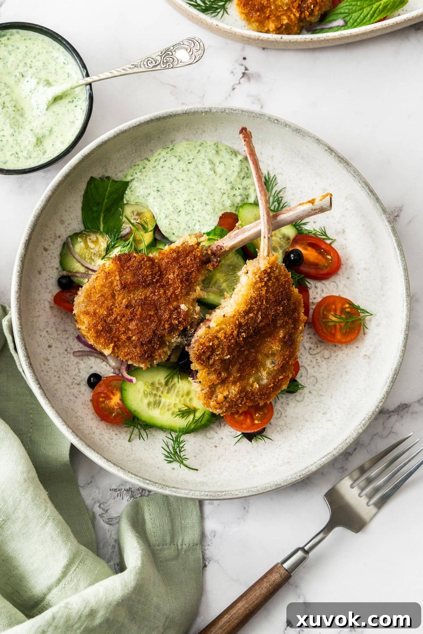 Two perfectly cooked crumbed lamb cutlets served on a dinner plate with fresh salad and a dollop of mint mayo.