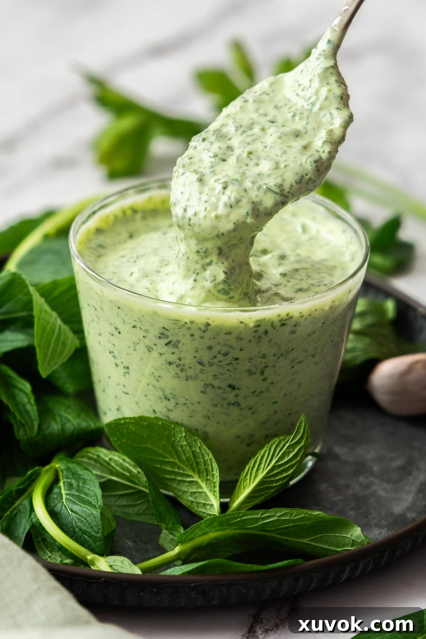 A spoon delicately drizzling vibrant minted mayo into a tall glass, showcasing its creamy texture.