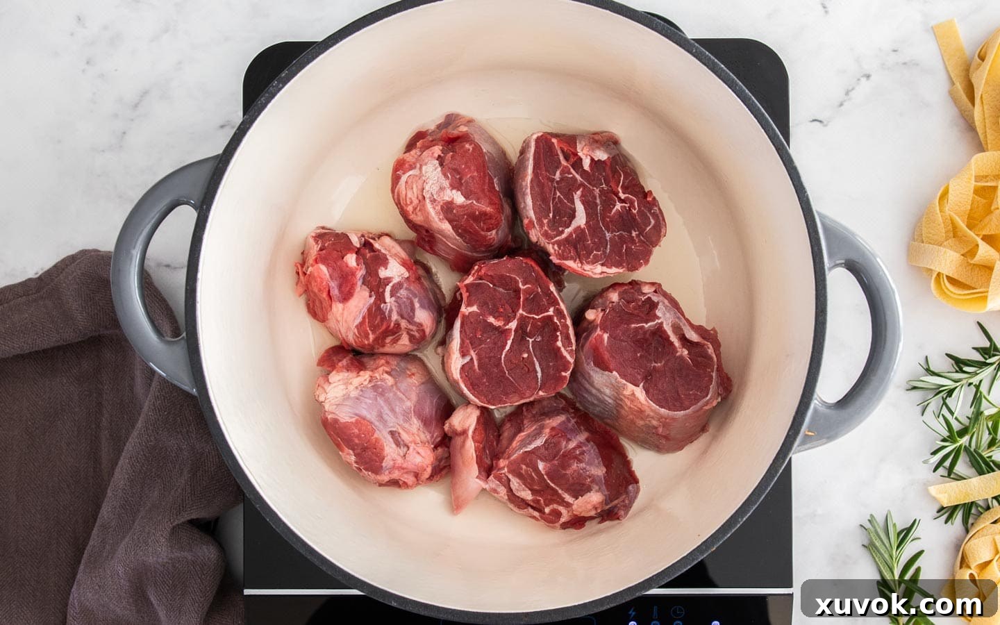 Raw pieces of beef shin in a pan, just starting to brown underneath.