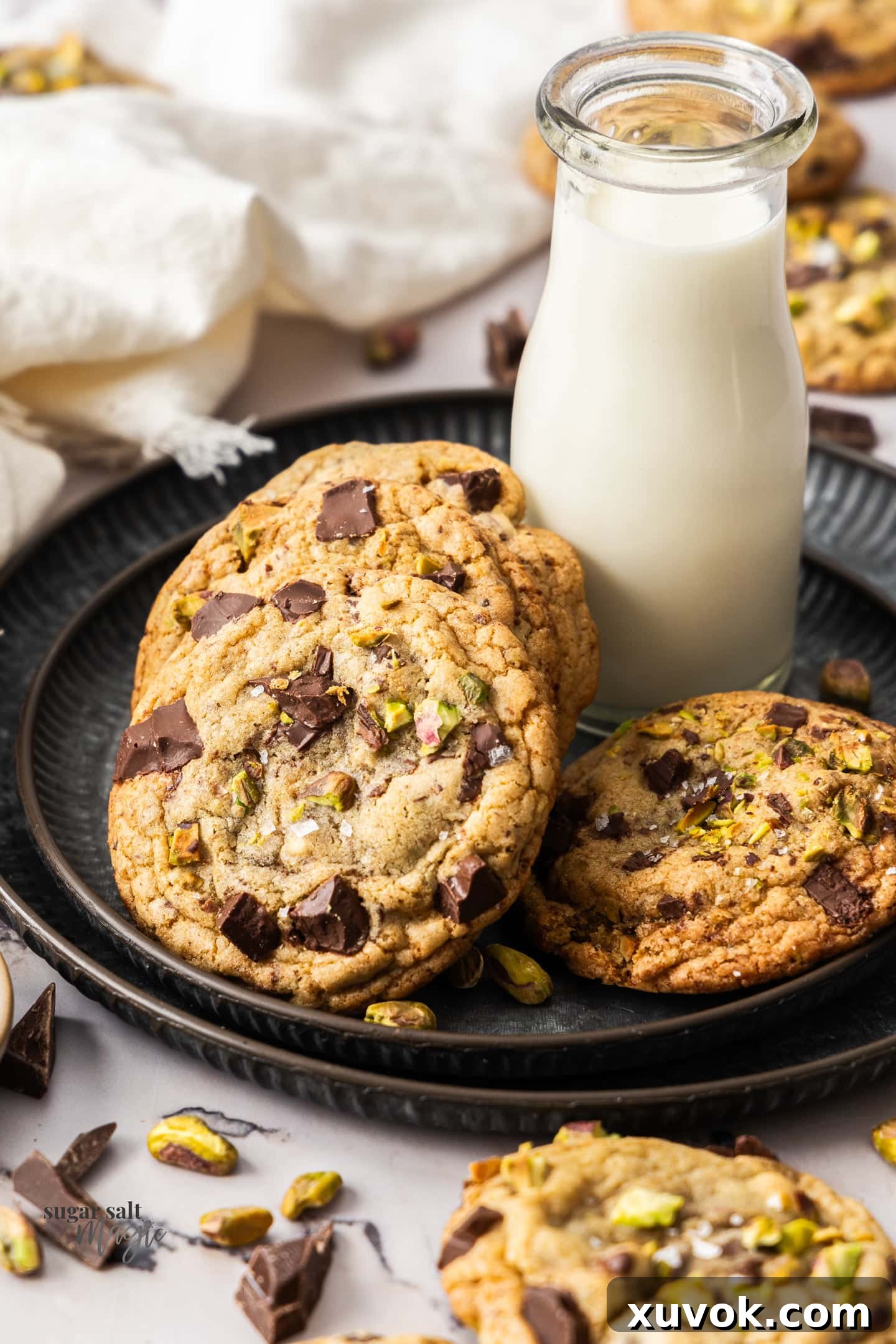 Chocolate chip pistachio cookies with a mini jug of milk on a metal platter.