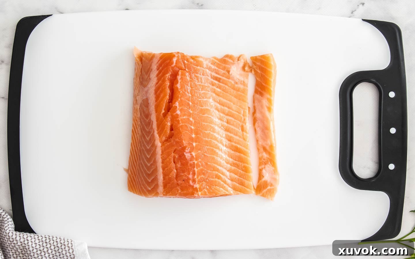 The salmon on a chopping board with a thin piece cut off the side to even out thickness.