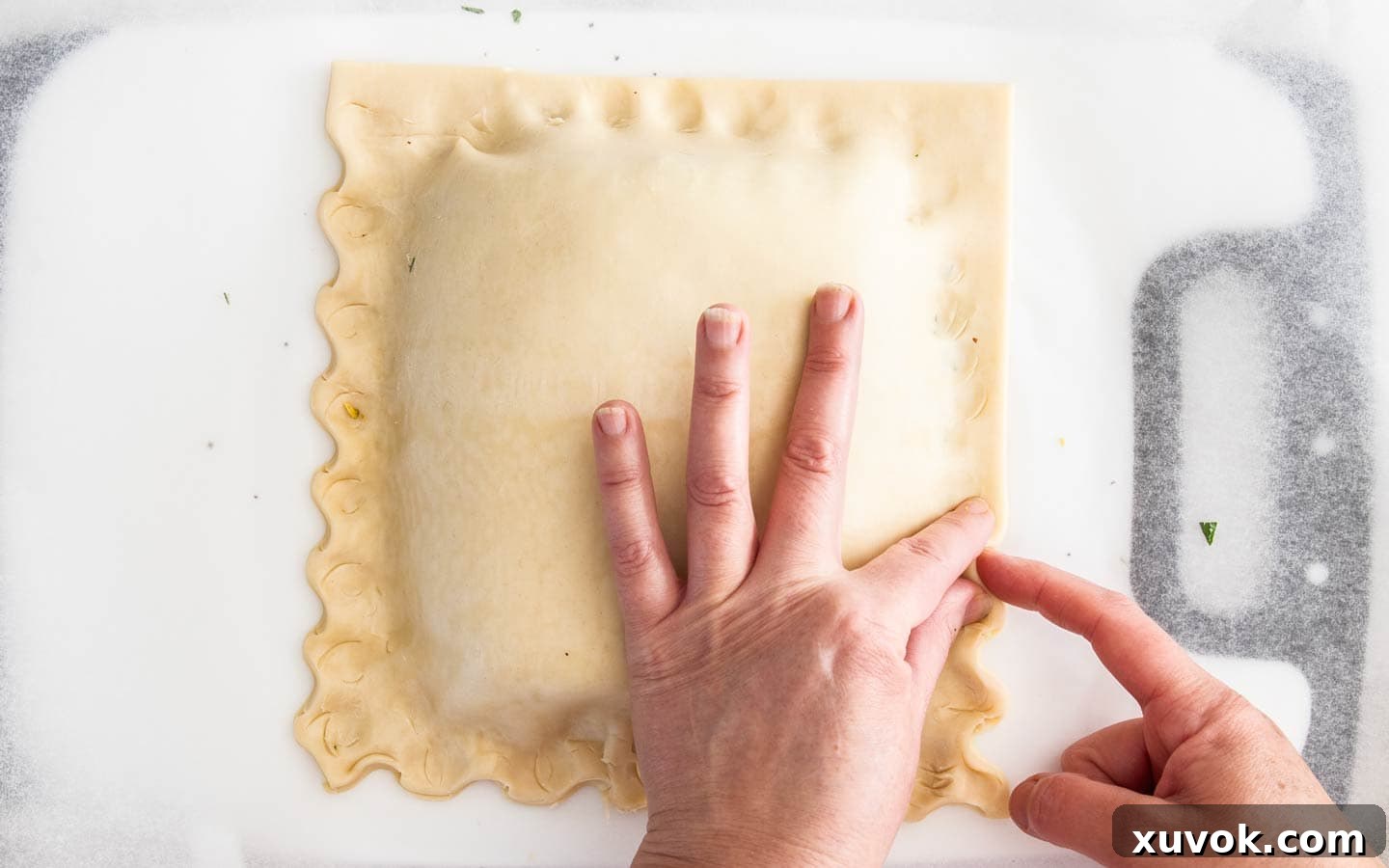 Hands crimping the edge of the salmon wellington, sealing the pastry.