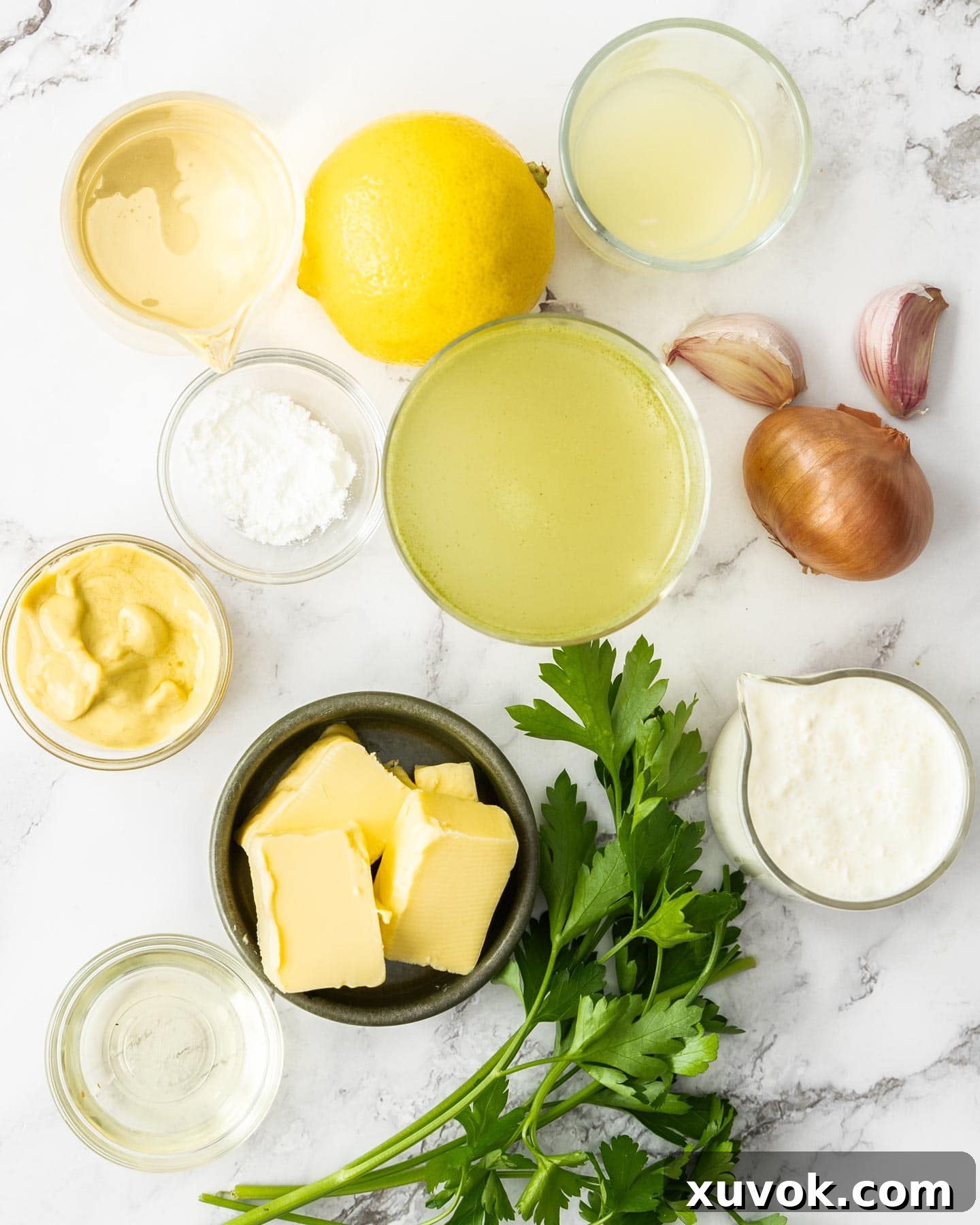 A selection of fresh ingredients for creamy white wine sauce, including shallots, garlic, lemon, a bottle of white wine, and a carton of cream, neatly arranged on a marble kitchen surface.