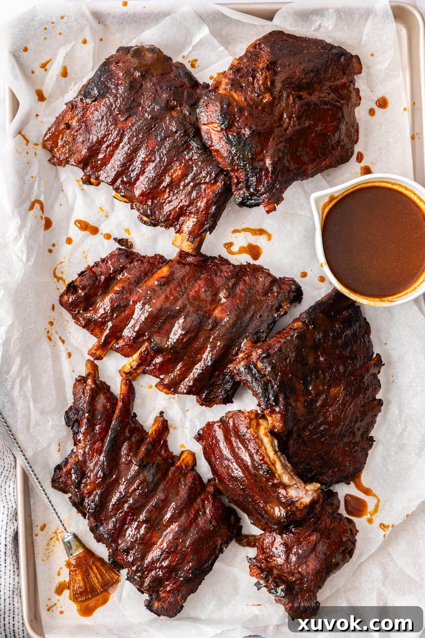 Six portions of tender BBQ slow cooker pork ribs arranged on a platter, with a small pot of extra sauce on the side.