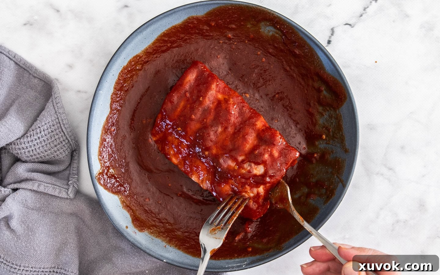 A hand basting raw pork ribs with the rich, homemade BBQ sauce before slow cooking.