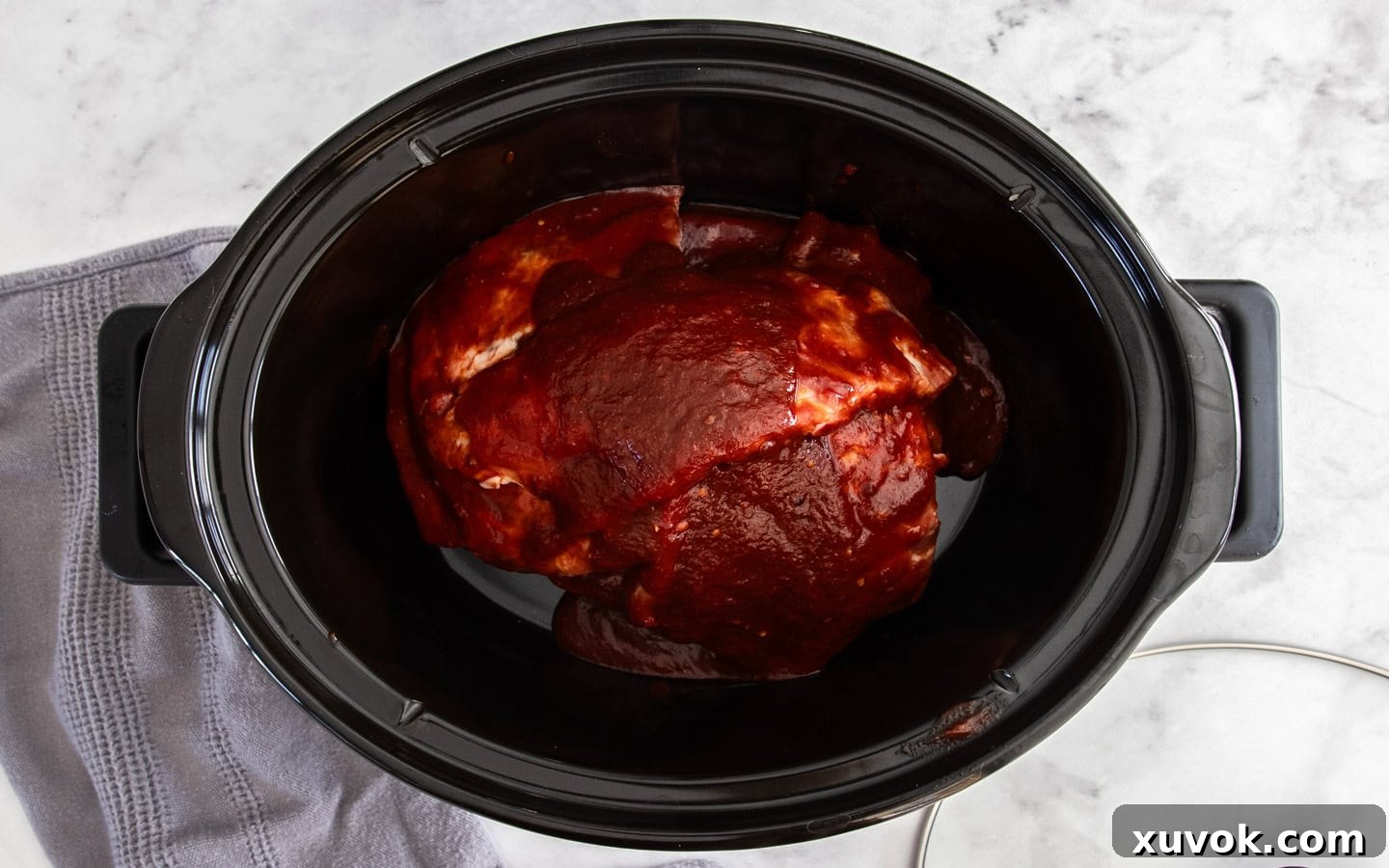 Prepared pork ribs, fully coated in BBQ sauce, neatly stacked inside a slow cooker bowl, ready for cooking.