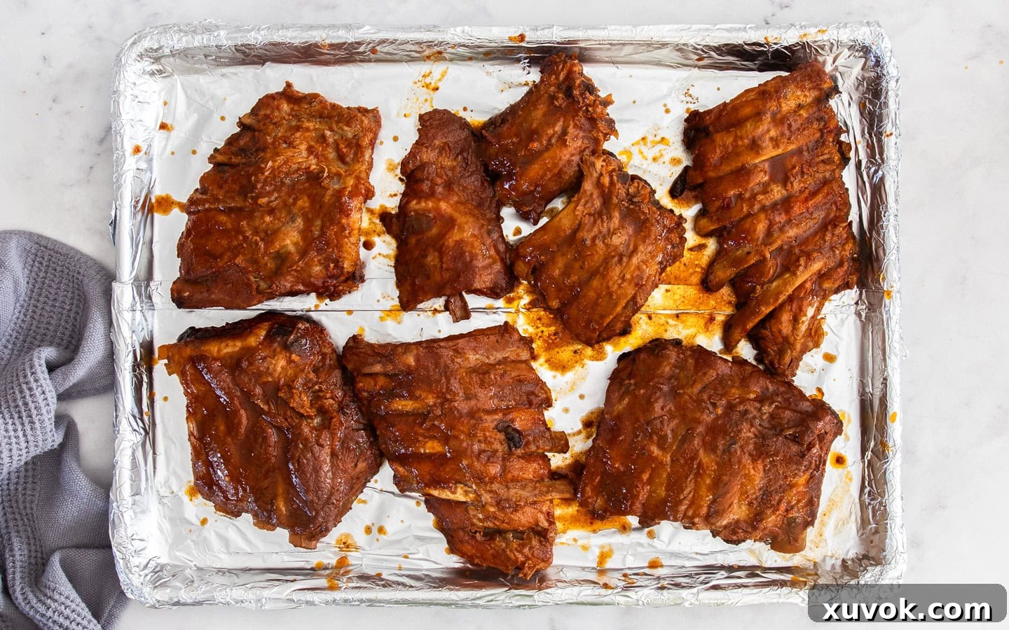 Cooked ribs arranged on a foil-lined baking tray, ready to be grilled for a caramelized finish.