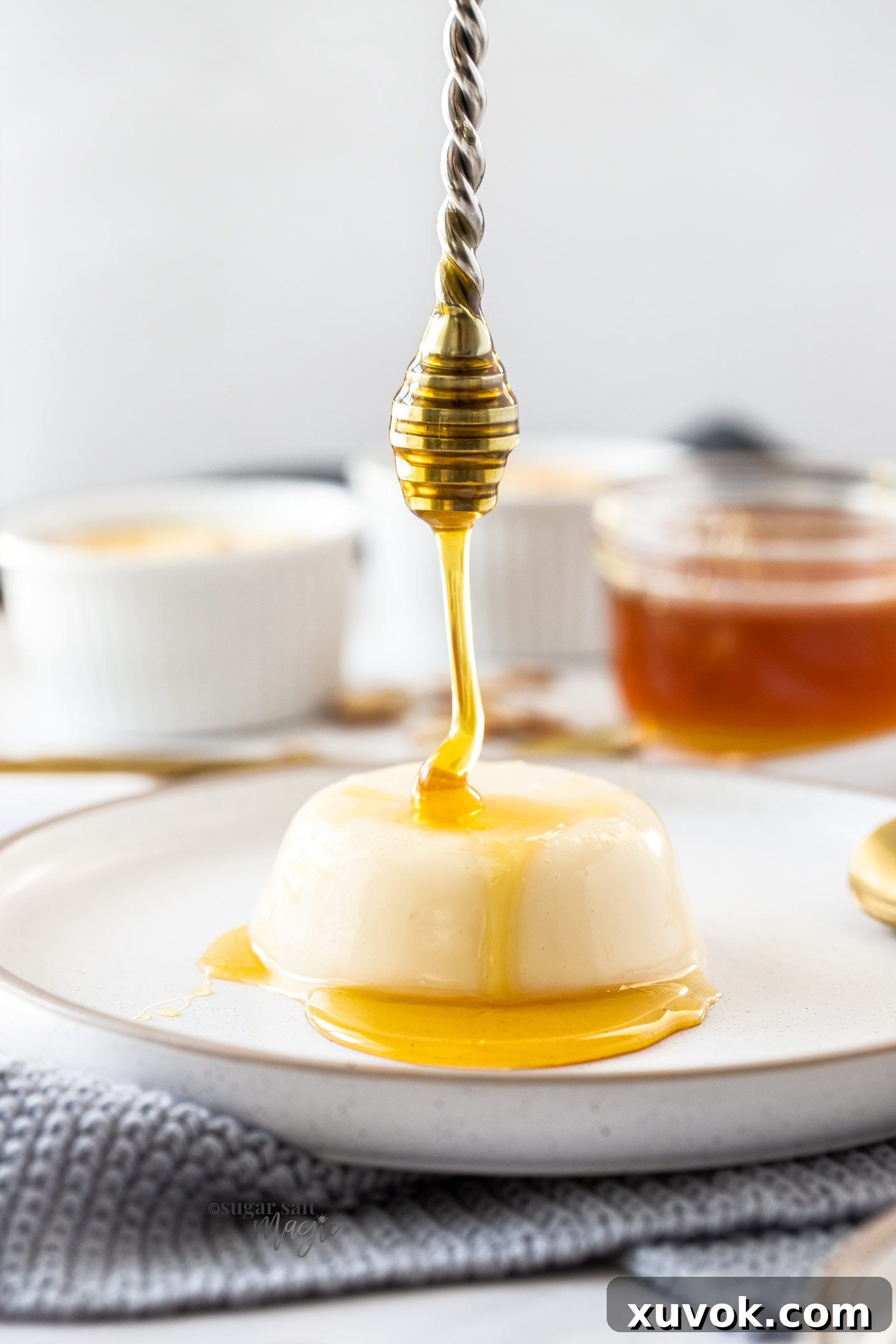Close-up of honey being drizzled over a smooth, creamy panna cotta on a white plate.