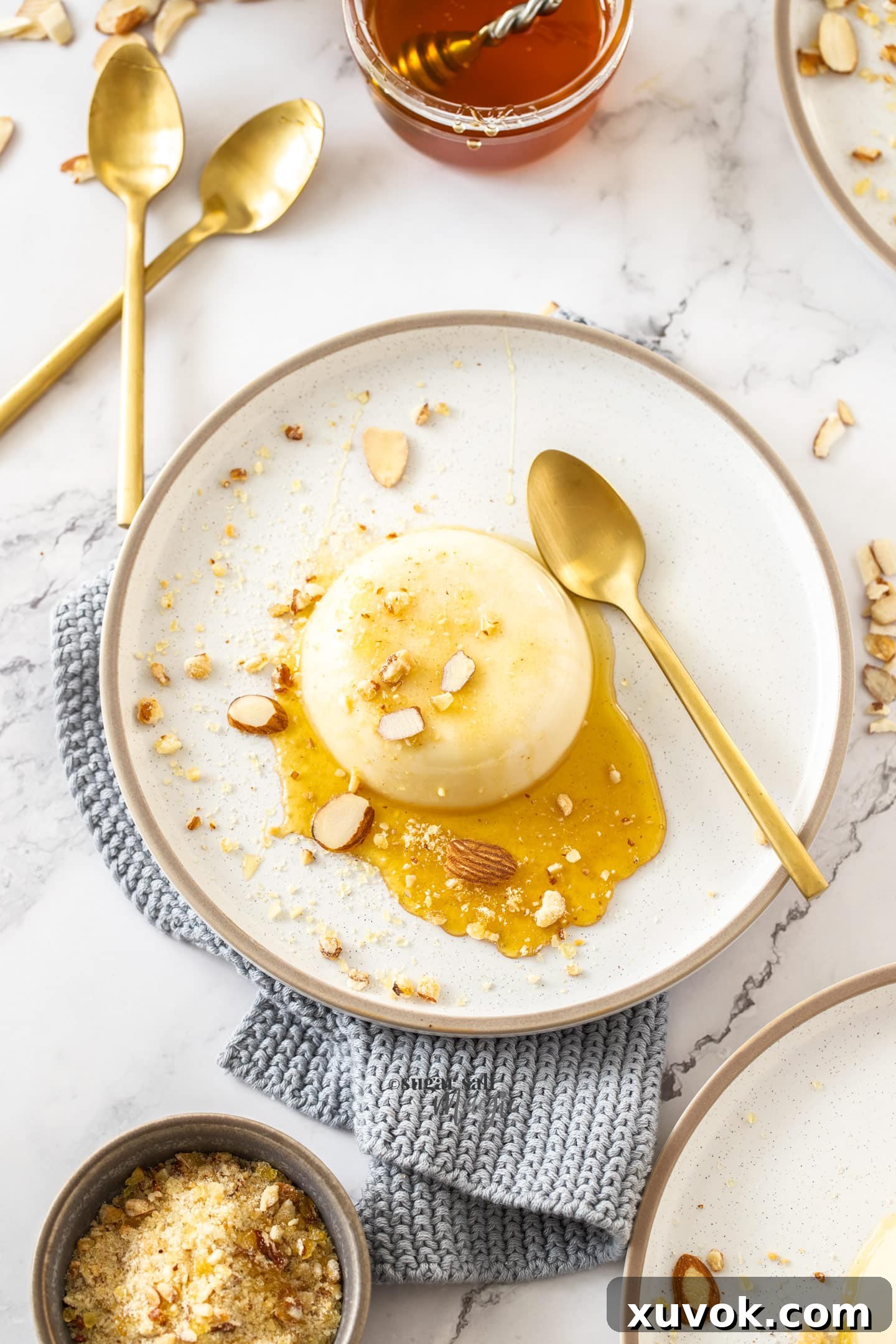 An overhead view of a honey panna cotta on a plate, garnished with honey and nuts.