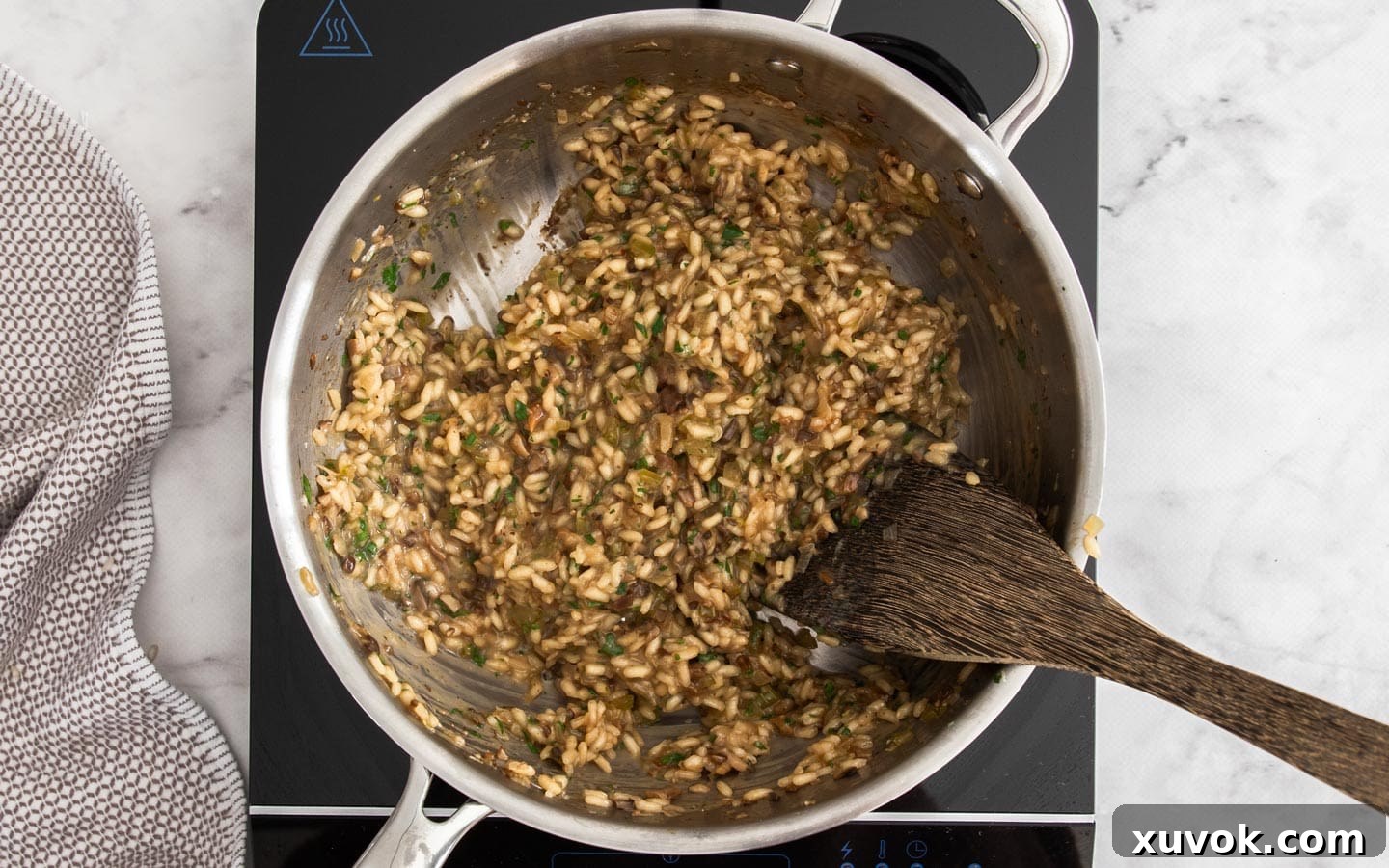 Cooked mushroom risotto in a pan, glistening with melted Parmesan cheese and flecked with fresh green parsley.