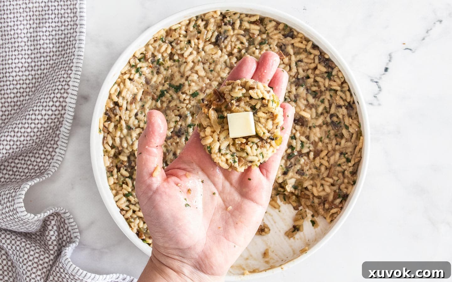 A flattened "puck" of mushroom risotto with a cube of mozzarella cheese positioned in its center, ready to be rolled.
