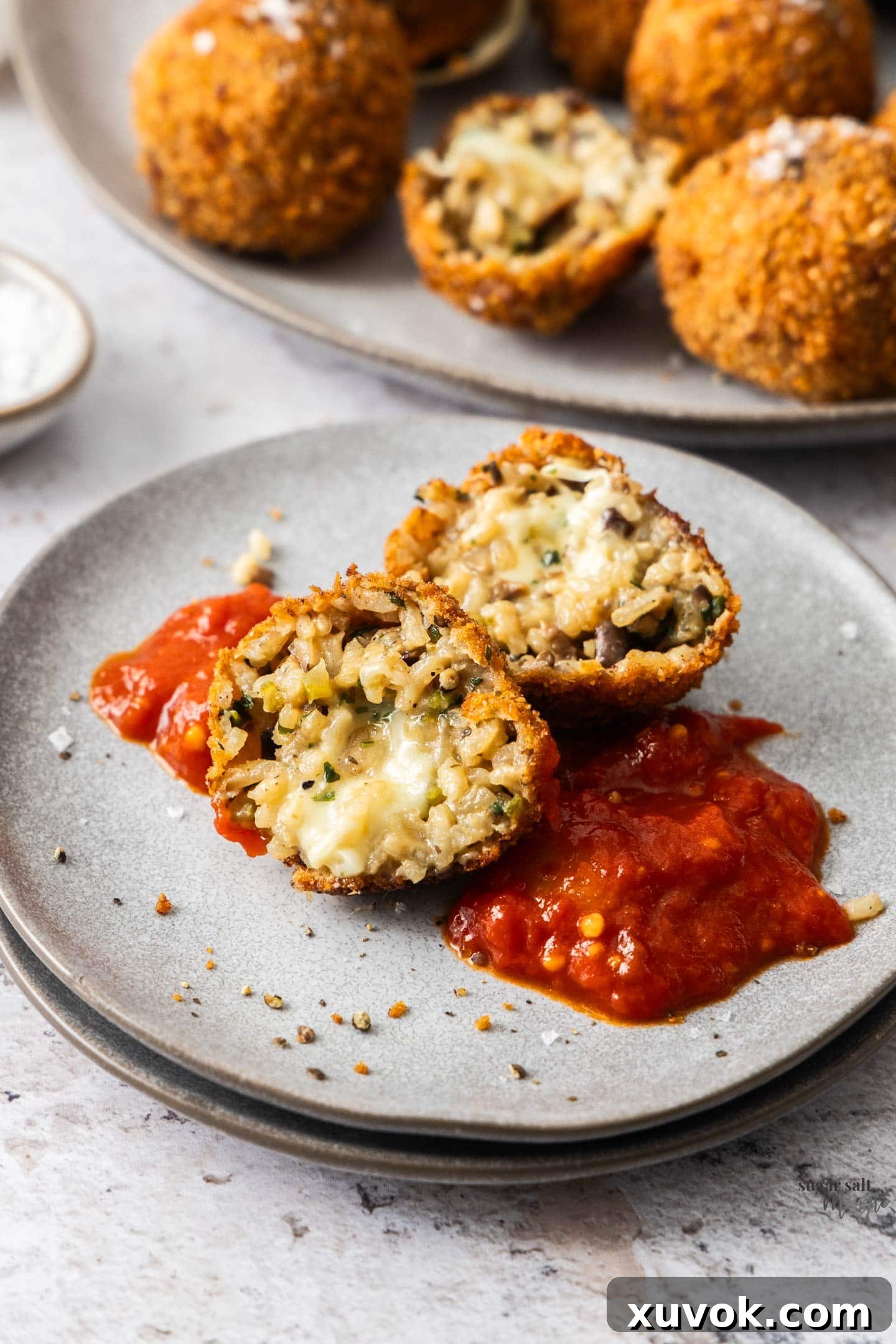 A perfectly fried mushroom arancini, cut open to reveal its creamy mushroom risotto and melted mozzarella, resting on a plate with a dollop of arrabbiata sauce.