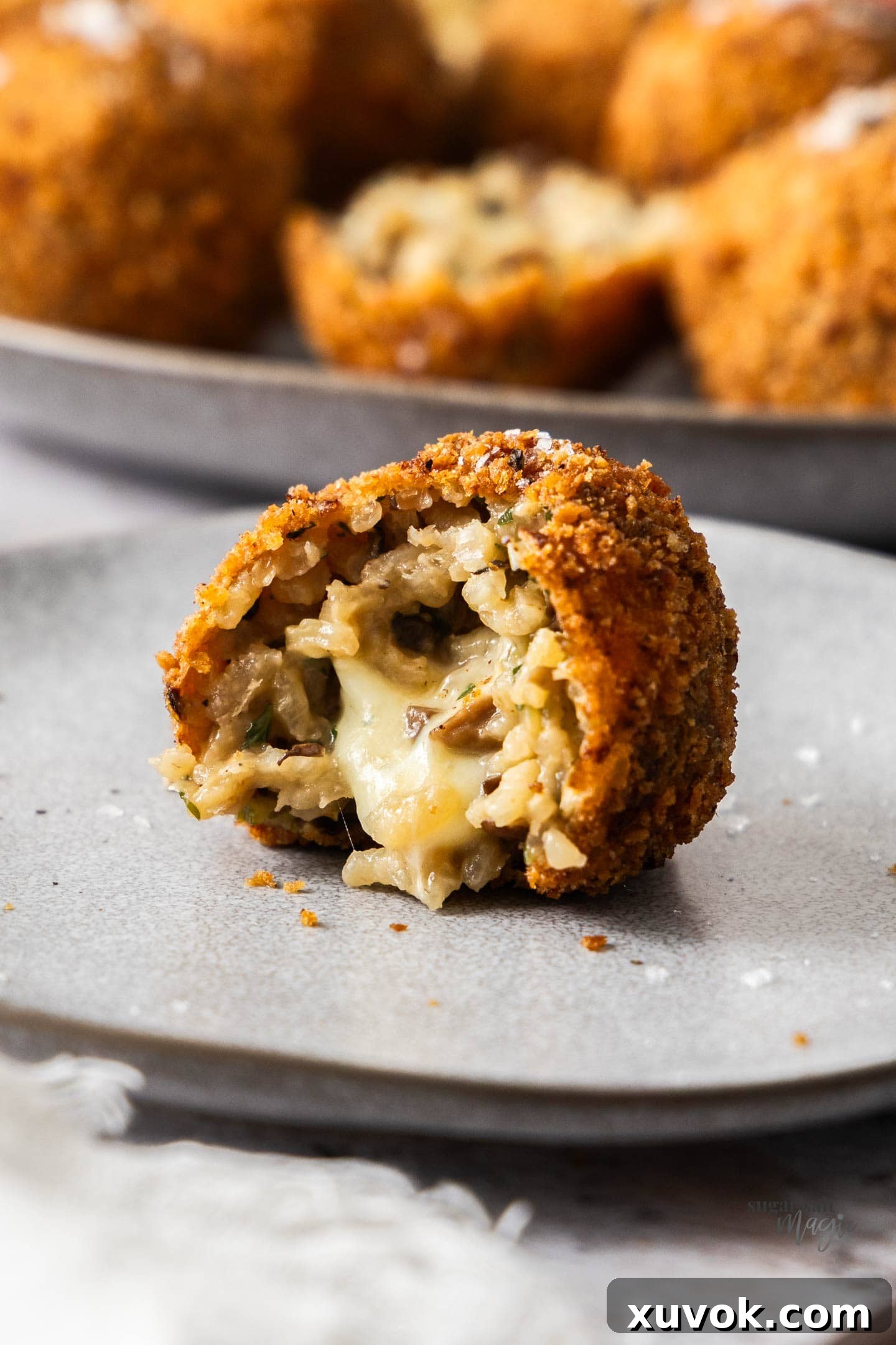 A close-up view of a mushroom arancini, perfectly split open to reveal the steam rising from its creamy risotto and stretchy, melted mozzarella core.