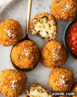Top down view of mushroom arancini on a plate with one on a spoon and one broken in half.