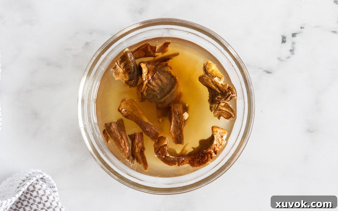 Dried porcini mushrooms soaking in hot stock in a small white bowl, capturing their earthy essence.