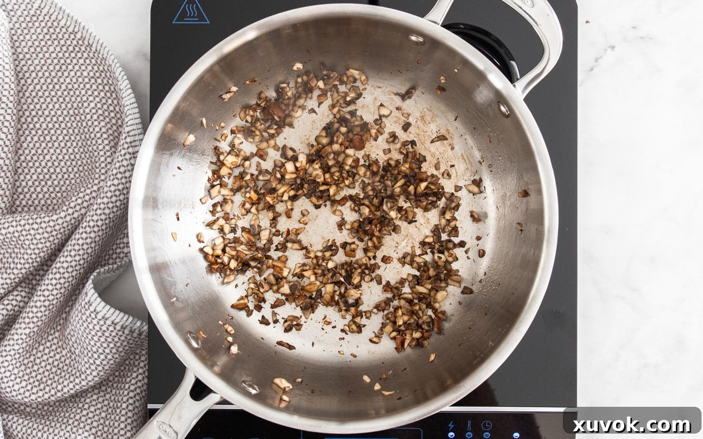 Finely chopped fresh mushrooms actively frying in a skillet over medium-high heat, beginning to brown and release their moisture.