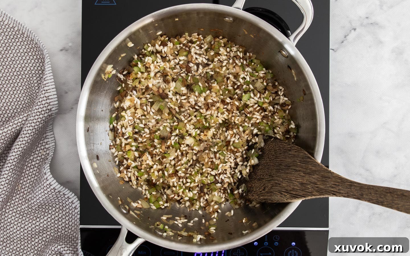 Arborio rice mixed with sautéed vegetables and mushrooms in a pan, with some grains starting to look glassy and translucent.