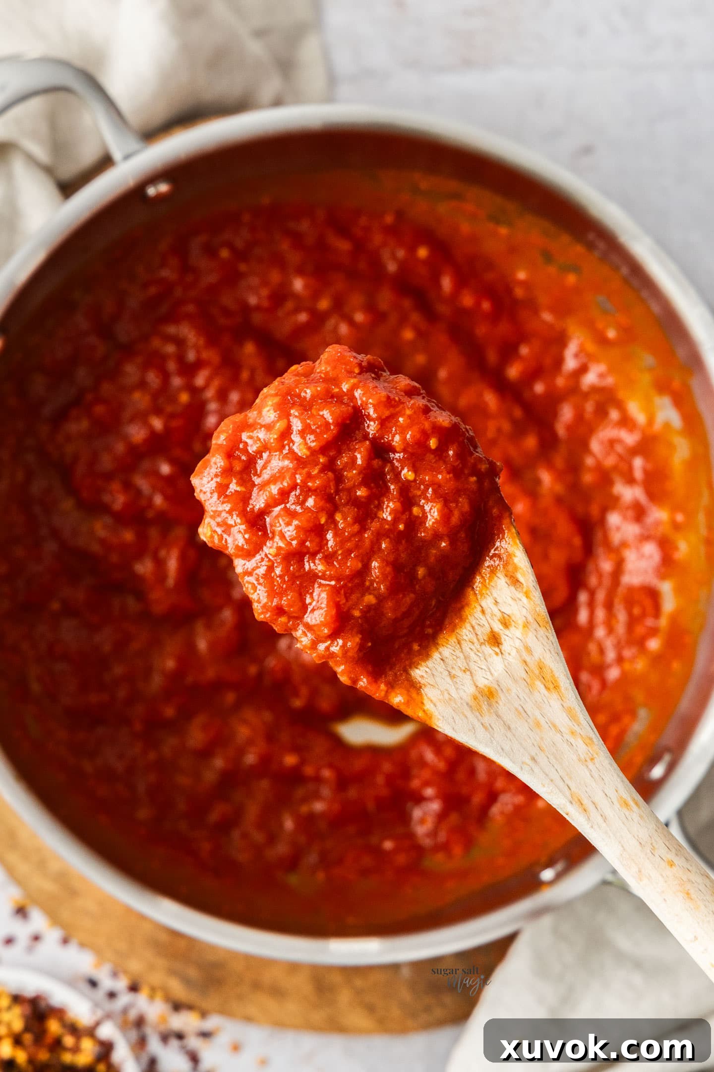A wooden spoon lifted from a pan, full of chunky arrabbiata sauce.