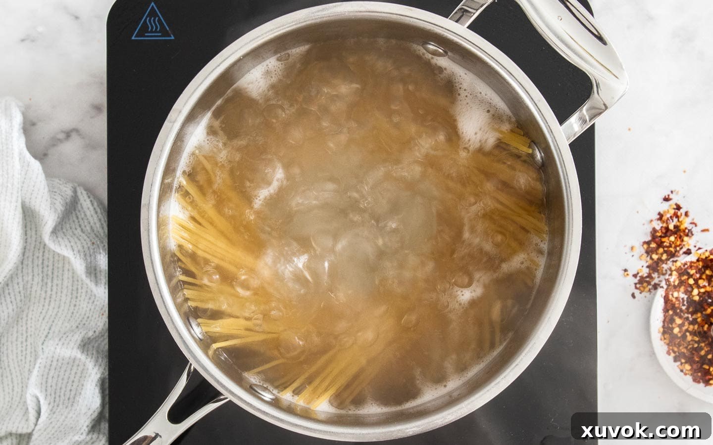 Spaghetti strands boiling vigorously in a large pot of salted water on the stovetop.