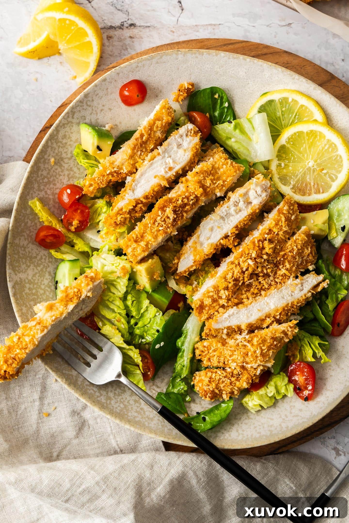 A panko chicken breast cut into slices, resting on a fresh green salad.