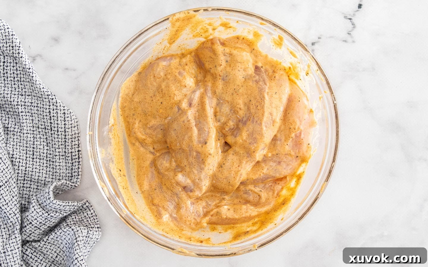 Chicken in a bowl, fully coated in the marinade mixture.